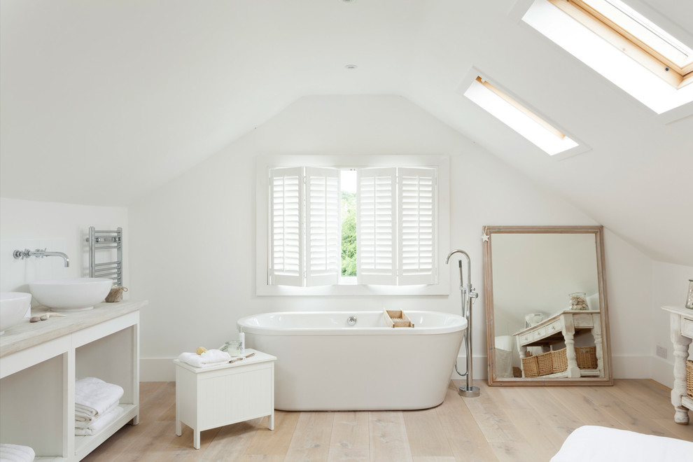 Beach style master bathroom in London with open cabinets, white cabinets, a freestanding tub, white walls, light hardwood floors, a vessel sink and wood benchtops.