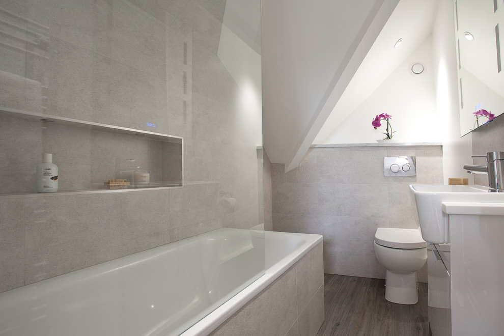 Inspiration for a small traditional 3/4 bathroom in Sussex with flat-panel cabinets, white cabinets, a drop-in tub, a shower/bathtub combo, a wall-mount toilet, gray tile, marble, grey walls, laminate floors, an integrated sink and grey floor.