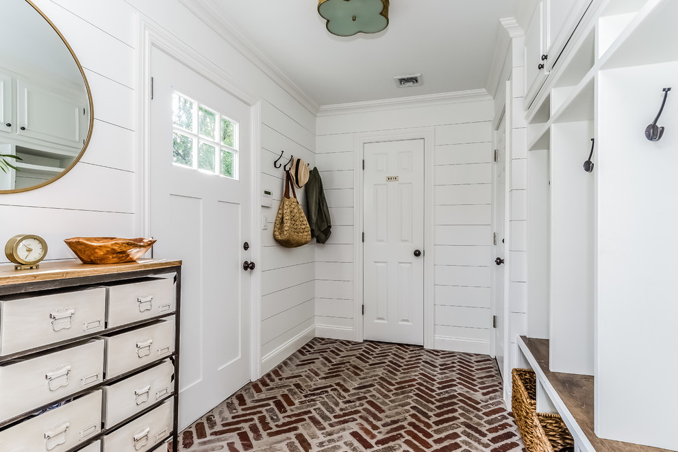 This is an example of a large traditional mudroom in New York with white walls, brick floors, a single front door, a white front door and red floor.