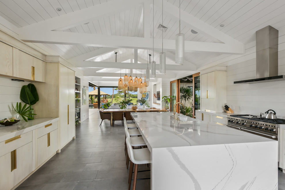 Large beach style galley open plan kitchen in Hawaii with a farmhouse sink, flat-panel cabinets, white cabinets, quartz benchtops, white splashback, stone slab splashback, stainless steel appliances, ceramic floors, with island and grey floor.