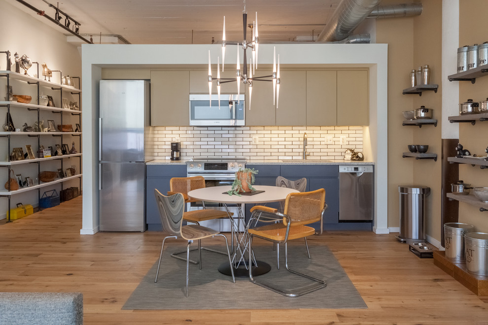 This is an example of a small industrial single-wall eat-in kitchen in Philadelphia with an undermount sink, flat-panel cabinets, quartz benchtops, white splashback, subway tile splashback, stainless steel appliances, medium hardwood floors, no island, brown floor and blue cabinets.