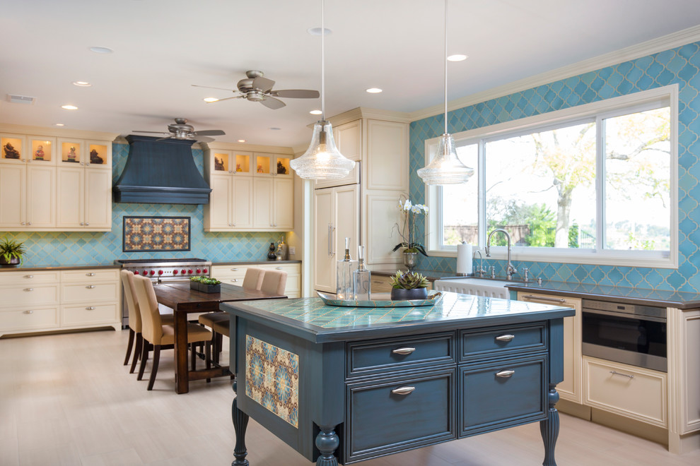 Large mediterranean l-shaped open plan kitchen in San Diego with a farmhouse sink, recessed-panel cabinets, yellow cabinets, quartz benchtops, blue splashback, porcelain splashback, stainless steel appliances, porcelain floors and with island.