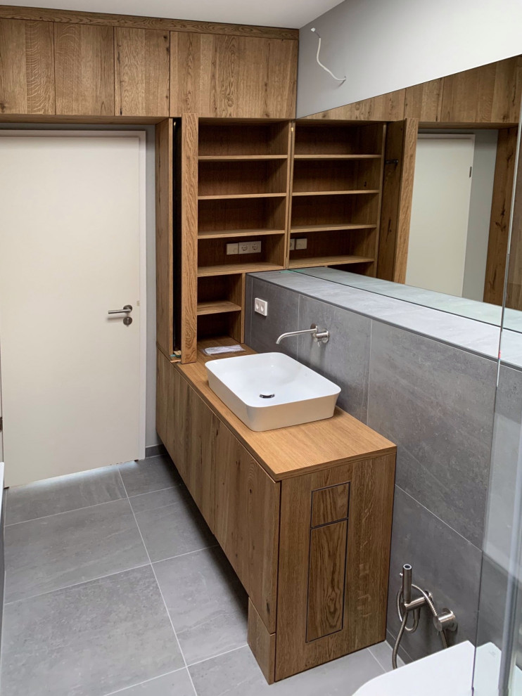 Exempel på ett mellanstort modernt badrum, med släta luckor, skåp i mörkt trä, en vägghängd toalettstol, grå kakel, keramikplattor, grå väggar och dusch med skjutdörr