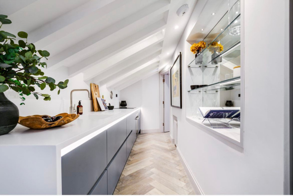 This is an example of a small modern single-wall separate kitchen in London with a single-bowl sink, flat-panel cabinets, blue cabinets, solid surface benchtops, white splashback, engineered quartz splashback, black appliances, light hardwood floors, no island, yellow benchtop and exposed beam.