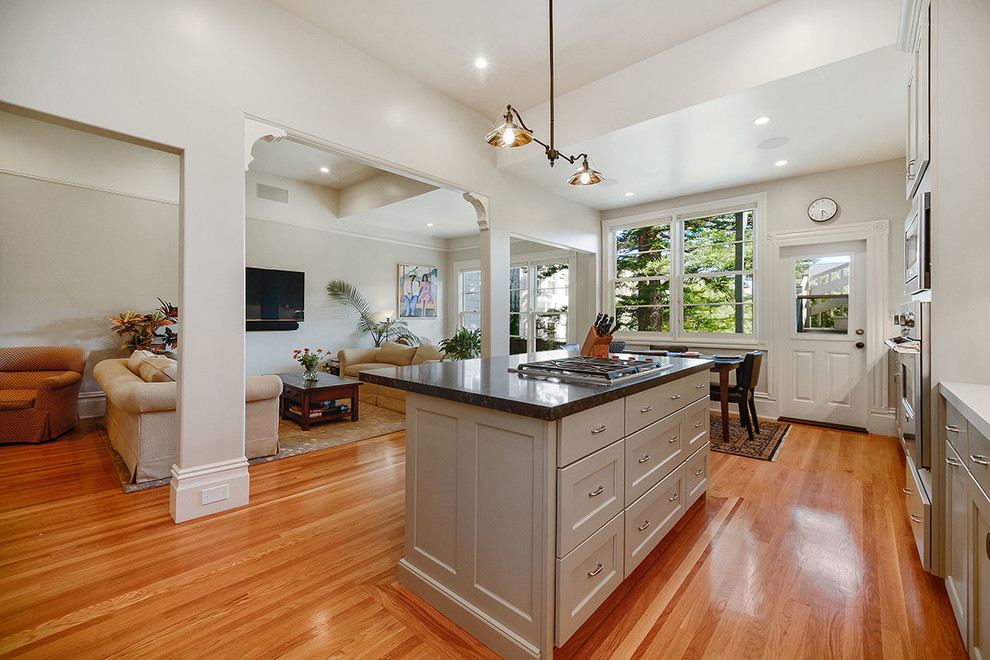Photo of a mid-sized traditional l-shaped eat-in kitchen in San Francisco with white cabinets, quartz benchtops, stainless steel appliances, medium hardwood floors, with island, an undermount sink, recessed-panel cabinets, white splashback and brown floor.