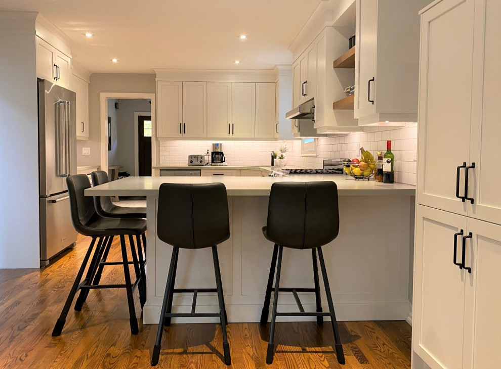 Inspiration for a mid-sized transitional u-shaped medium tone wood floor and brown floor open concept kitchen remodel in Toronto with an undermount sink, shaker cabinets, white cabinets, quartz countertops, white backsplash, porcelain backsplash, stainless steel appliances, a peninsula and gray countertops