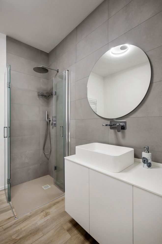 Стильный дизайн: маленькая ванная комната в современном стиле с плоскими фасадами, белыми фасадами, угловым душем, инсталляцией, серой плиткой, керамогранитной плиткой, белыми стенами, деревянным полом, душевой кабиной, настольной раковиной, столешницей из искусственного камня, душем с распашными дверями, белой столешницей, тумбой под одну раковину и подвесной тумбой для на участке и в саду - последний тренд