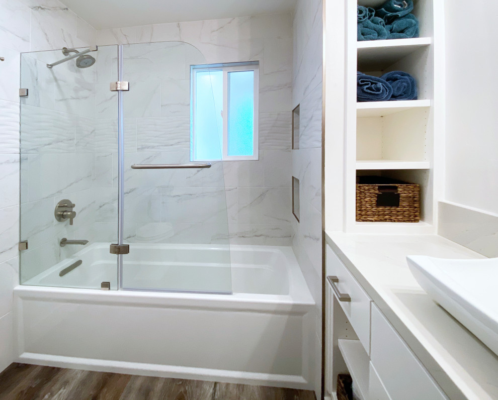 Alcove bathtub - mid-sized transitional 3/4 black and white tile and porcelain tile vinyl floor, brown floor and single-sink alcove bathtub idea with shaker cabinets, white cabinets, a two-piece toilet, white walls, a vessel sink, quartz countertops, a hinged shower door, gray countertops, a niche and a built-in vanity