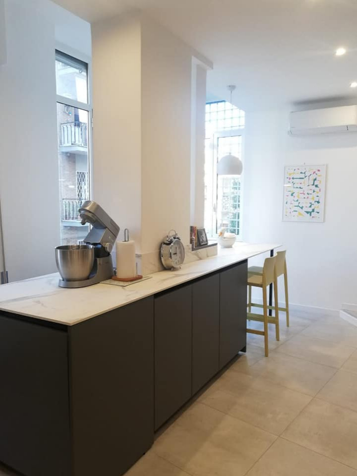 Photo of a large modern open plan kitchen in Rome with a drop-in sink, flat-panel cabinets, grey cabinets, solid surface benchtops, white splashback, stainless steel appliances, porcelain floors, with island and white benchtop.
