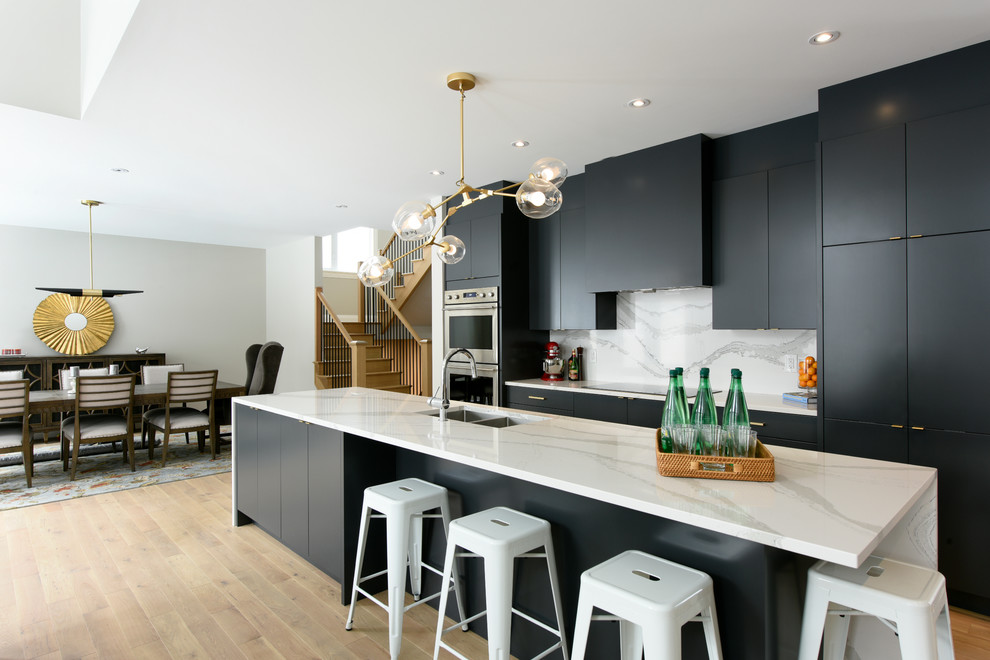Contemporary galley eat-in kitchen in Toronto with an undermount sink, flat-panel cabinets, black cabinets, white splashback, stone slab splashback, stainless steel appliances, medium hardwood floors, with island and brown floor.