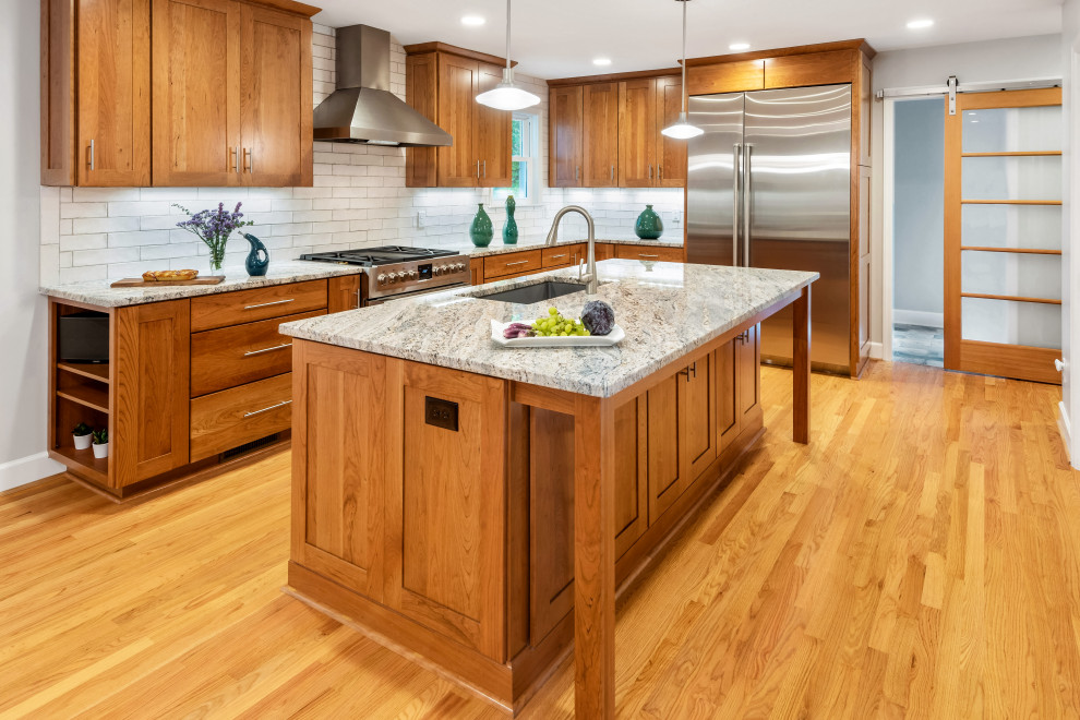 This is an example of a mid-sized transitional l-shaped open plan kitchen in Raleigh with an undermount sink, shaker cabinets, medium wood cabinets, granite benchtops, white splashback, subway tile splashback, stainless steel appliances, medium hardwood floors, with island, brown floor and white benchtop.
