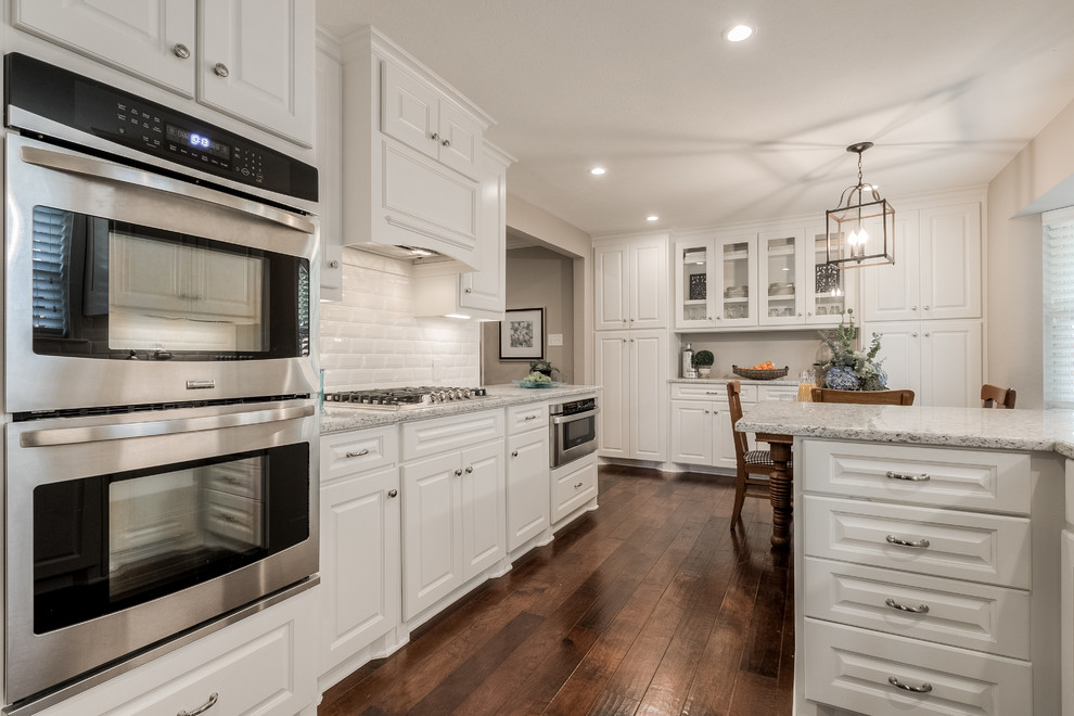 Enclosed kitchen - mid-sized transitional galley medium tone wood floor enclosed kitchen idea in Dallas with an undermount sink, raised-panel cabinets, white cabinets, granite countertops, white backsplash, subway tile backsplash, stainless steel appliances and a peninsula