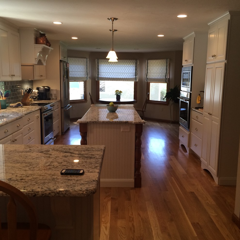 Inspiration for a transitional u-shaped medium tone wood floor eat-in kitchen remodel in Boston with an undermount sink, raised-panel cabinets, white cabinets, granite countertops, blue backsplash, glass tile backsplash, stainless steel appliances and an island