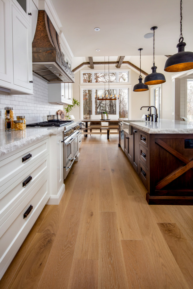 Example of a large mountain style l-shaped light wood floor and beige floor eat-in kitchen design in Toronto with a farmhouse sink, shaker cabinets, white cabinets, quartz countertops, white backsplash, subway tile backsplash, paneled appliances, an island and white countertops