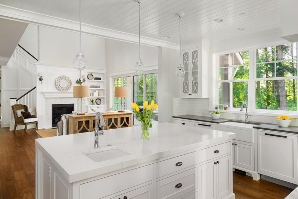 Inspiration for a mid-sized country u-shaped kitchen in Boston with a farmhouse sink, shaker cabinets, white cabinets, quartz benchtops, white splashback, subway tile splashback, stainless steel appliances, dark hardwood floors, with island, brown floor, white benchtop and wood.