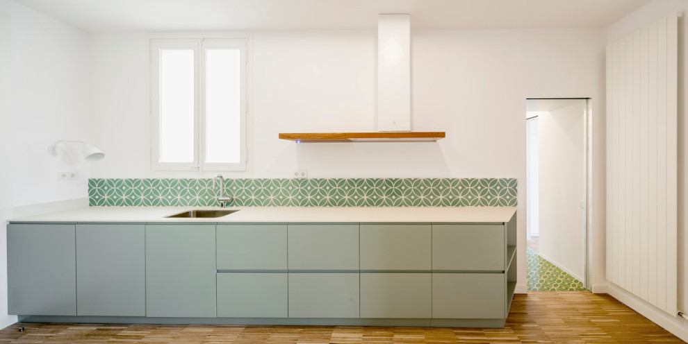 Inspiration for a mid-sized contemporary single-wall eat-in kitchen in Barcelona with an undermount sink, flat-panel cabinets, turquoise cabinets, green splashback, cement tile splashback, medium hardwood floors, no island, multi-coloured floor and white benchtop.