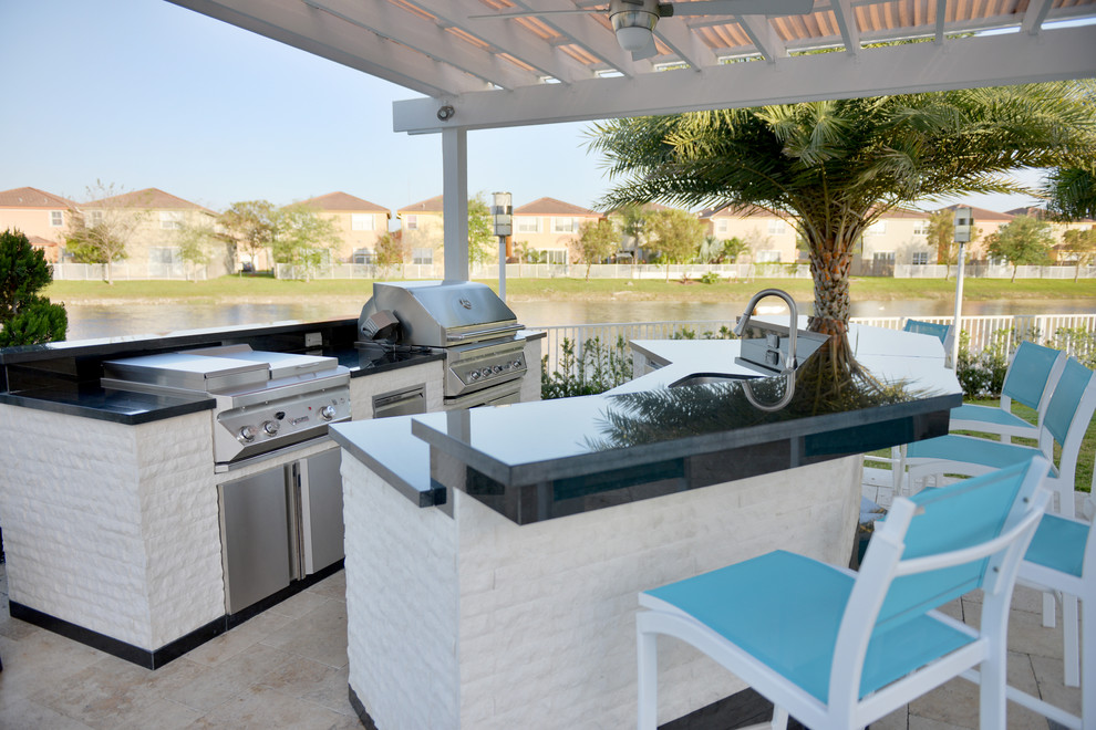 Photo of an expansive tropical backyard patio in Miami with an outdoor kitchen, natural stone pavers and a pergola.