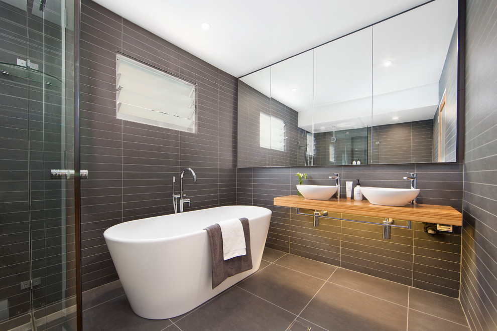 Design ideas for a modern master bathroom in Sydney with a freestanding tub, a corner shower, gray tile, grey walls, porcelain floors, wood benchtops, grey floor, a hinged shower door, subway tile and a vessel sink.