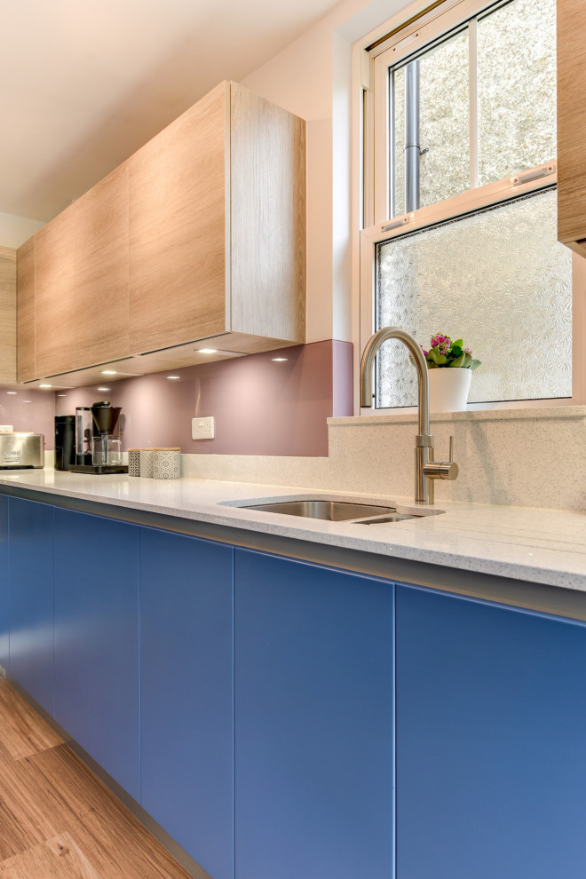 Eat-in kitchen - mid-sized coastal l-shaped dark wood floor and brown floor eat-in kitchen idea in Sussex with a double-bowl sink, flat-panel cabinets, blue cabinets, quartzite countertops, multicolored backsplash, glass sheet backsplash, black appliances, an island and white countertops