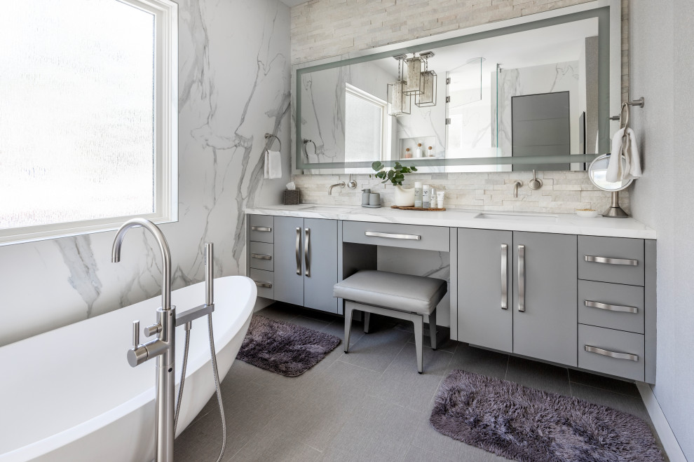 This is an example of a mid-sized contemporary master bathroom with flat-panel cabinets, grey cabinets, a freestanding tub, an alcove shower, a bidet, white tile, pebble tile, porcelain floors, an undermount sink, solid surface benchtops, grey floor, white benchtops, a double vanity, a built-in vanity, an enclosed toilet and wallpaper.