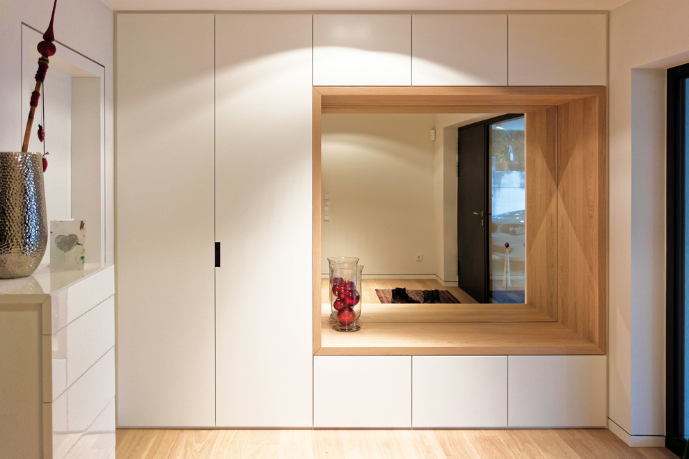 This is an example of an expansive contemporary mudroom in Frankfurt with white walls, light hardwood floors and a single front door.