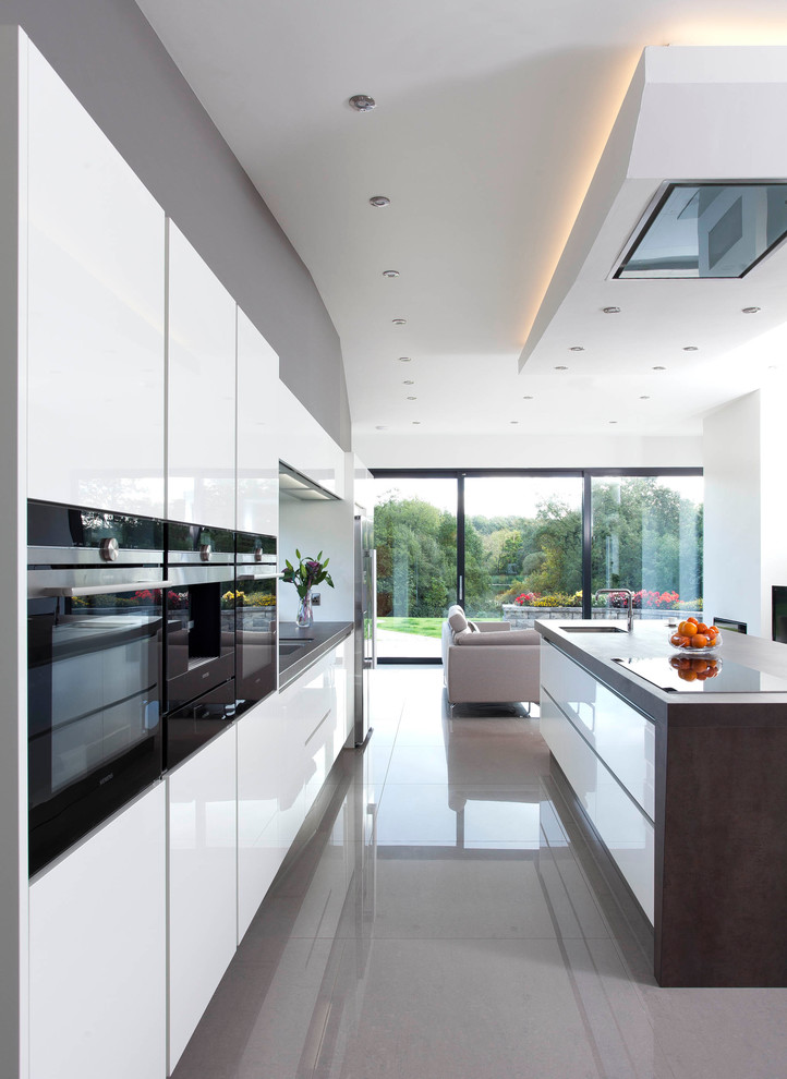 Inspiration for a large contemporary single-wall open plan kitchen in Belfast with an integrated sink, flat-panel cabinets, white cabinets, quartz benchtops, grey splashback, stone slab splashback, stainless steel appliances, porcelain floors and with island.