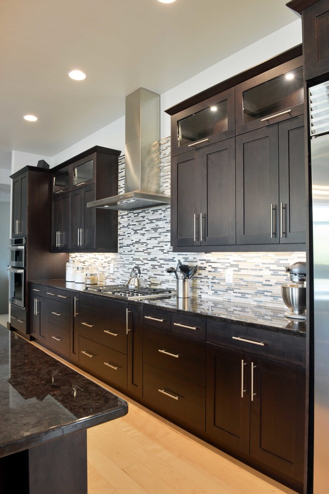 Open concept kitchen - large transitional l-shaped light wood floor and beige floor open concept kitchen idea with an undermount sink, shaker cabinets, dark wood cabinets, quartz countertops, multicolored backsplash, glass sheet backsplash, stainless steel appliances and an island