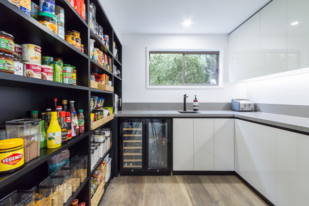 Expansive contemporary u-shaped eat-in kitchen in Melbourne with flat-panel cabinets, quartz benchtops, white splashback, stainless steel appliances, porcelain floors, with island, brown floor, an undermount sink, white cabinets and grey benchtop.