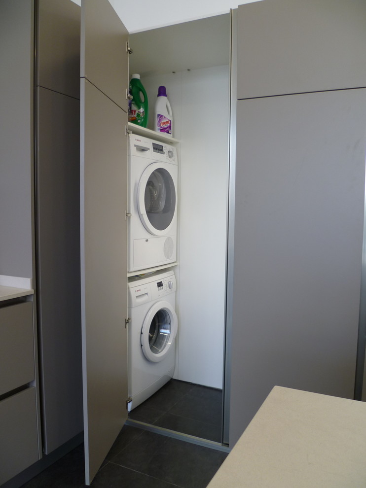 Photo of a small contemporary single-wall laundry cupboard in Other with flat-panel cabinets, grey cabinets and a stacked washer and dryer.
