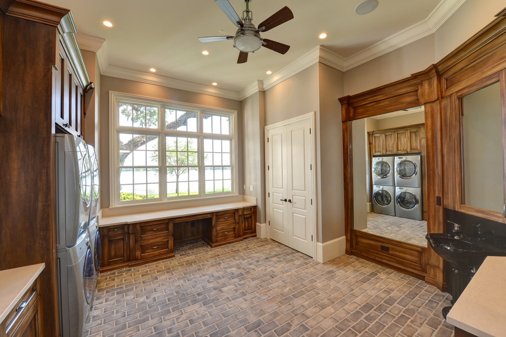Inspiration for a large transitional utility room in Orlando with an integrated sink, recessed-panel cabinets, quartzite benchtops, beige walls, brick floors, a stacked washer and dryer, grey floor and medium wood cabinets.