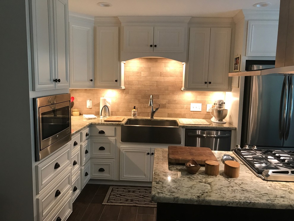 Example of a large transitional l-shaped brown floor eat-in kitchen design in Birmingham with a farmhouse sink, recessed-panel cabinets, white cabinets, beige backsplash, stainless steel appliances and an island