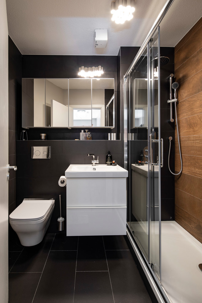 This is an example of a small contemporary master bathroom in Dublin with flat-panel cabinets, white cabinets, an alcove shower, a wall-mount toilet, brown tile, ceramic tile, black walls, ceramic floors, a wall-mount sink, tile benchtops, black floor, a sliding shower screen and black benchtops.