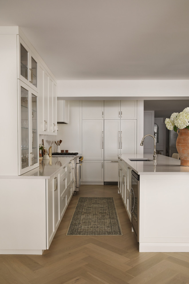This is an example of a mid-sized transitional l-shaped eat-in kitchen in Montreal with an undermount sink, raised-panel cabinets, white cabinets, quartz benchtops, white splashback, engineered quartz splashback, stainless steel appliances, light hardwood floors, with island and white benchtop.
