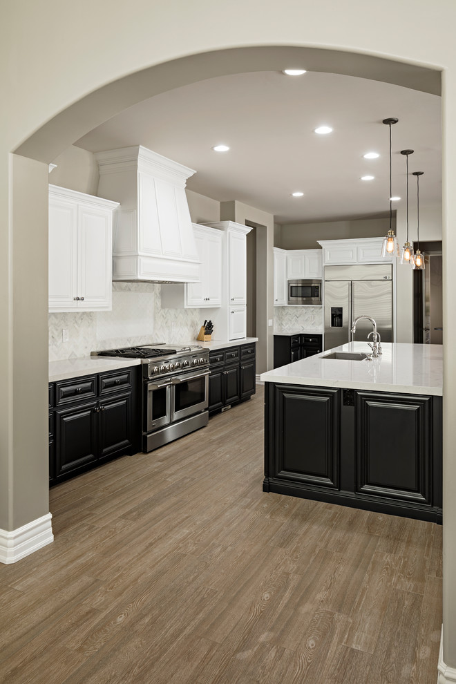 Large transitional l-shaped light wood floor and brown floor open concept kitchen photo in Phoenix with an undermount sink, raised-panel cabinets, black cabinets, quartz countertops, white backsplash, marble backsplash, stainless steel appliances and an island