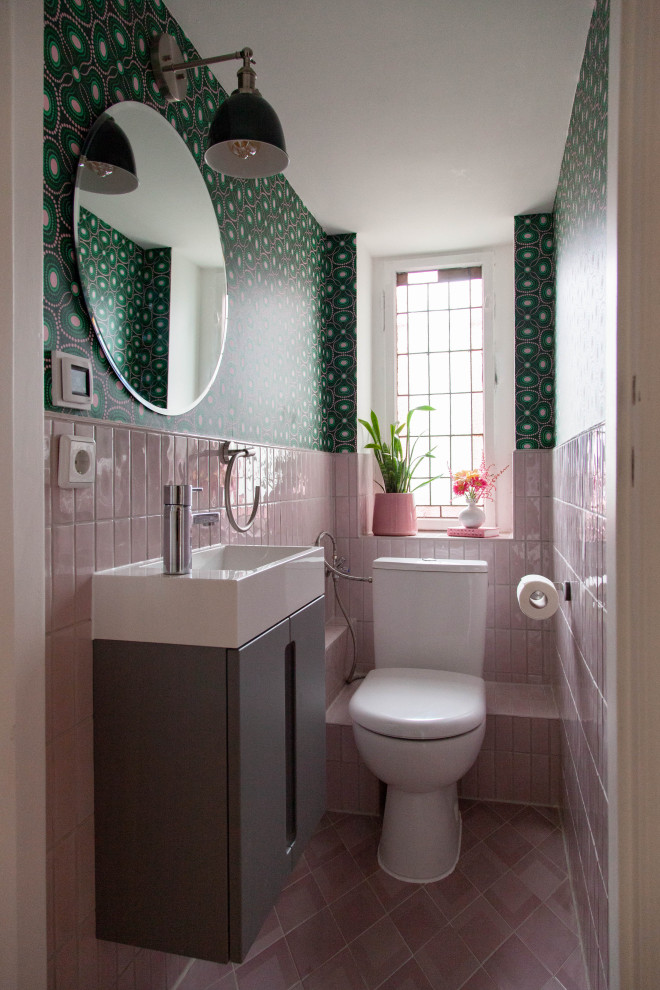 This is an example of a small eclectic master bathroom in Berlin with flat-panel cabinets, grey cabinets, a one-piece toilet, pink tile, ceramic tile, green walls, ceramic floors, an integrated sink, laminate benchtops, pink floor, white benchtops, an enclosed toilet, a single vanity, a floating vanity and wallpaper.