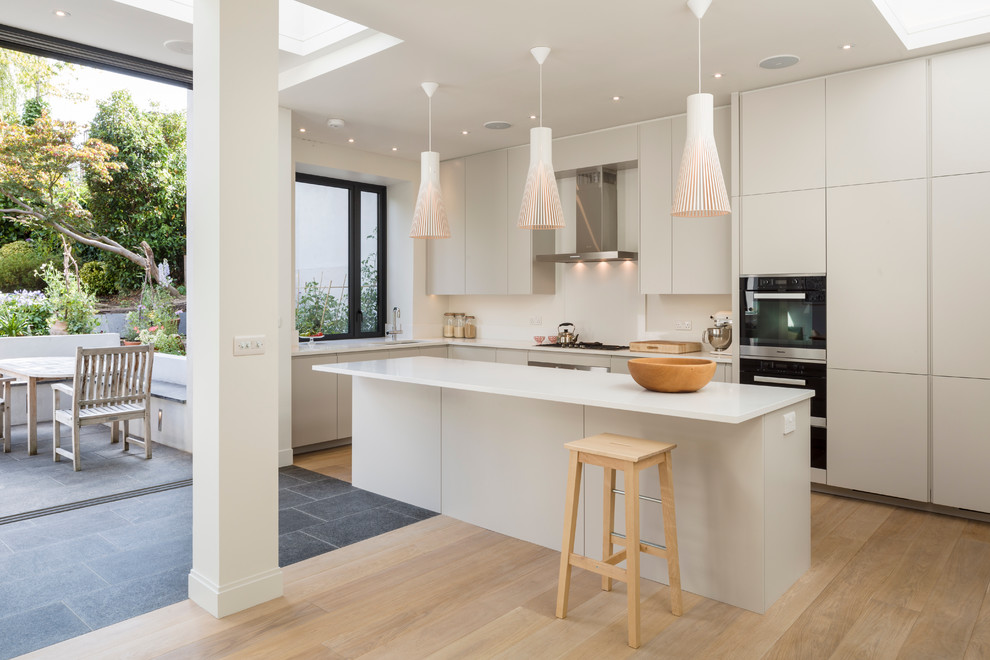 Photo of a scandinavian kitchen in London with with island, flat-panel cabinets, quartz benchtops, stainless steel appliances, an undermount sink, light hardwood floors and grey cabinets.
