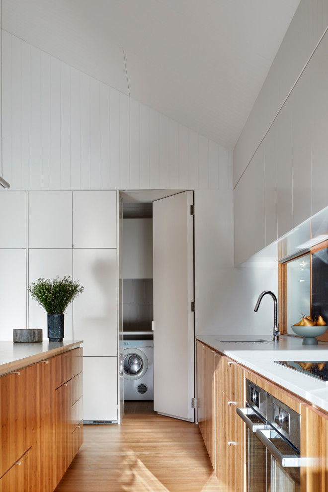Modern inredning av ett stort vit vitt kök, med en undermonterad diskho, luckor med infälld panel, skåp i ljust trä, bänkskiva i kvarts, rostfria vitvaror, ljust trägolv, en köksö och brunt golv