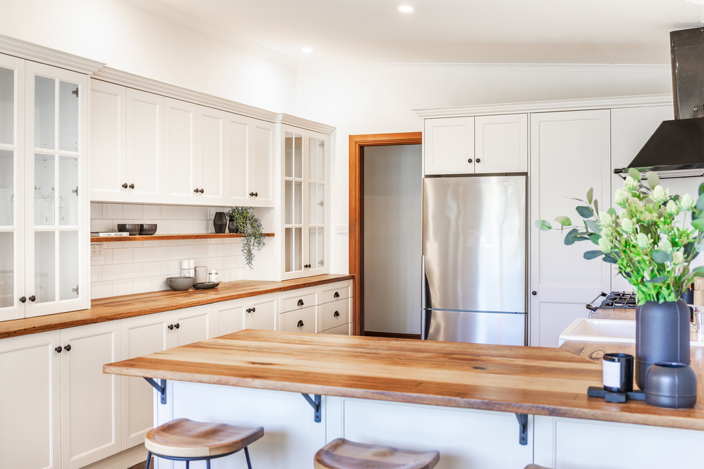 Design ideas for a mid-sized country l-shaped eat-in kitchen in Adelaide with a farmhouse sink, shaker cabinets, white cabinets, wood benchtops, white splashback, subway tile splashback, black appliances, slate floors, a peninsula, grey floor and yellow benchtop.