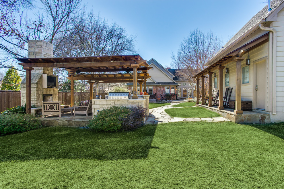 This is an example of a large country backyard patio in Dallas with an outdoor kitchen, natural stone pavers and a pergola.
