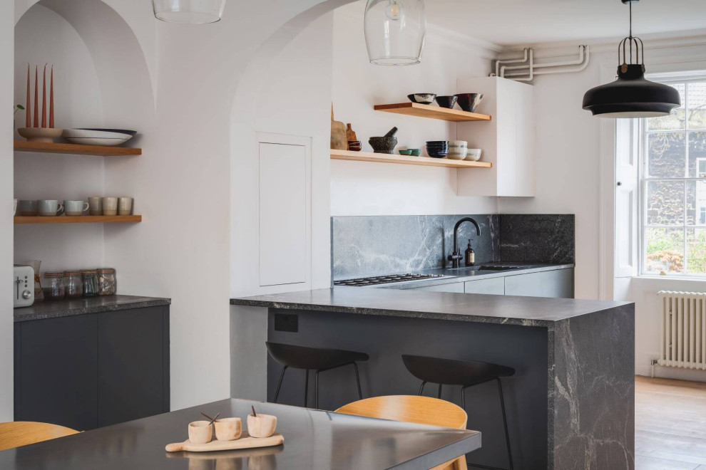 Inspiration for a mid-sized modern l-shaped open plan kitchen in Other with a single-bowl sink, flat-panel cabinets, black cabinets, granite benchtops, black splashback, granite splashback, black appliances and black benchtop.