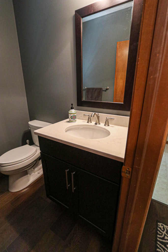 Cette image montre un petit WC et toilettes traditionnel avec un placard à porte plane, des portes de placard noires, WC séparés, un sol en vinyl, un lavabo encastré, un plan de toilette en quartz modifié, un sol marron, un plan de toilette blanc et meuble-lavabo sur pied.