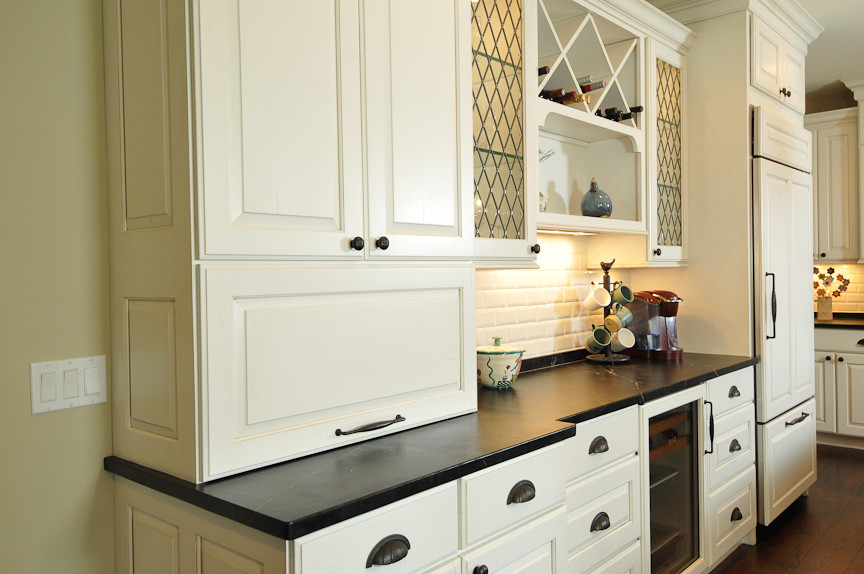 Eat-in kitchen - rustic l-shaped eat-in kitchen idea in Chicago with a farmhouse sink, raised-panel cabinets, white cabinets, soapstone countertops, white backsplash, subway tile backsplash and paneled appliances