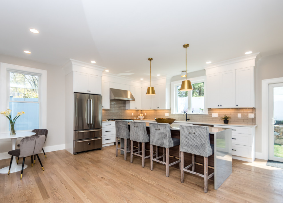 Mid-sized transitional l-shaped light wood floor and white floor open concept kitchen photo in Boston with an undermount sink, shaker cabinets, white cabinets, quartz countertops, gray backsplash, ceramic backsplash, stainless steel appliances, an island and white countertops