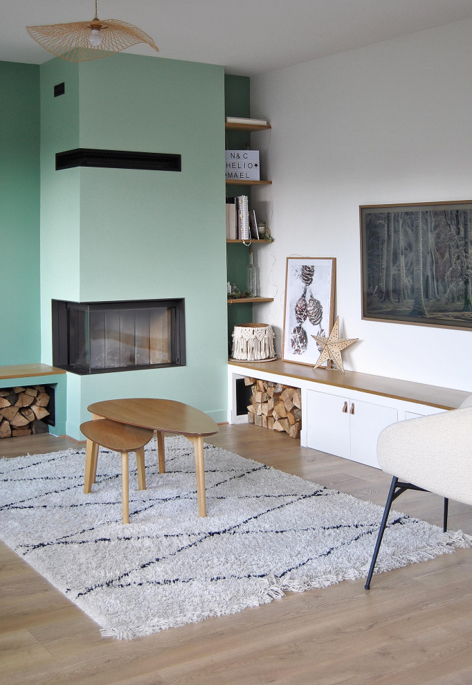 Mid-sized scandinavian open concept living room in Paris with a library, white walls, light hardwood floors, a corner fireplace, a plaster fireplace surround and a wall-mounted tv.