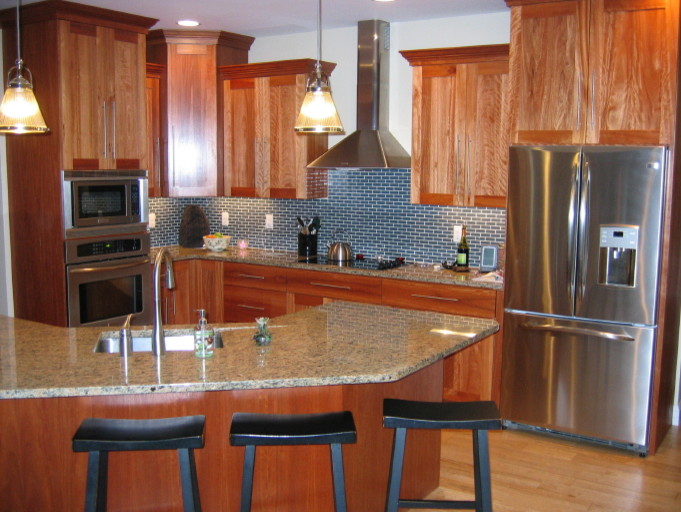 Photo of a mid-sized transitional u-shaped kitchen in Boston with recessed-panel cabinets, granite benchtops, a peninsula, medium wood cabinets, an undermount sink, blue splashback, stainless steel appliances and light hardwood floors.