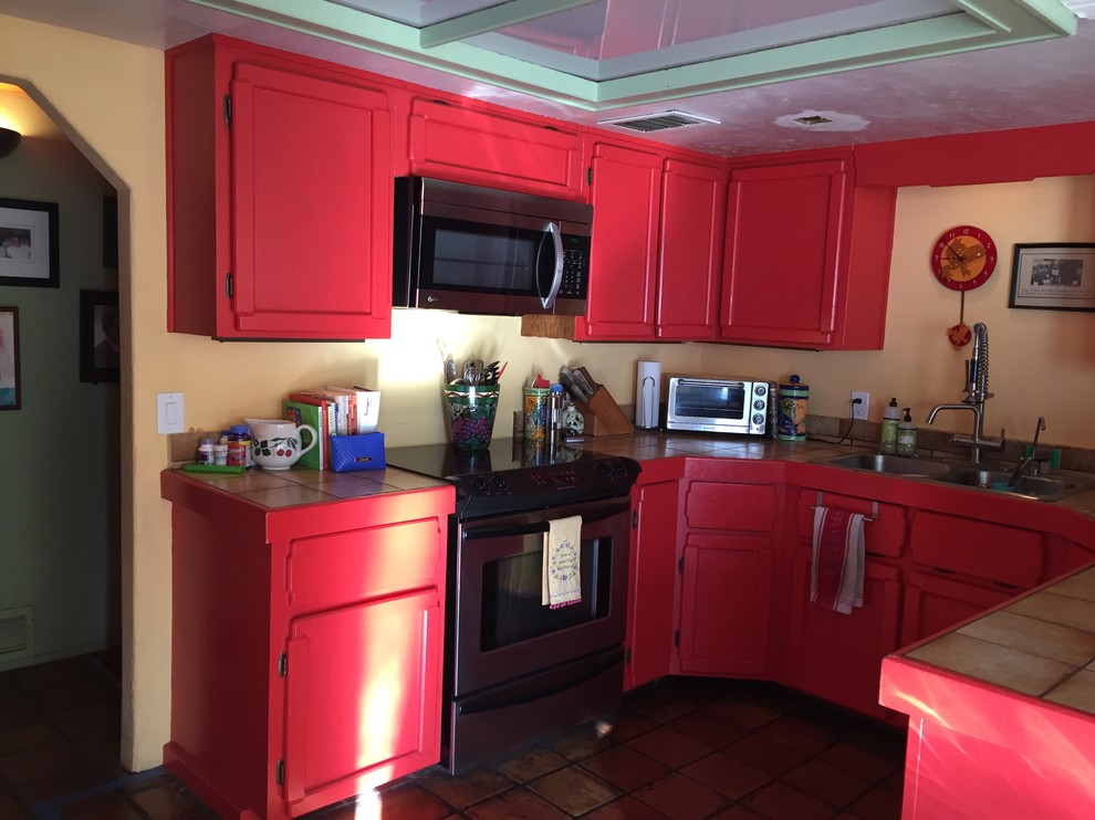 This is an example of a small contemporary u-shaped eat-in kitchen in Phoenix with a double-bowl sink, recessed-panel cabinets, red cabinets, tile benchtops, stainless steel appliances and terra-cotta floors.