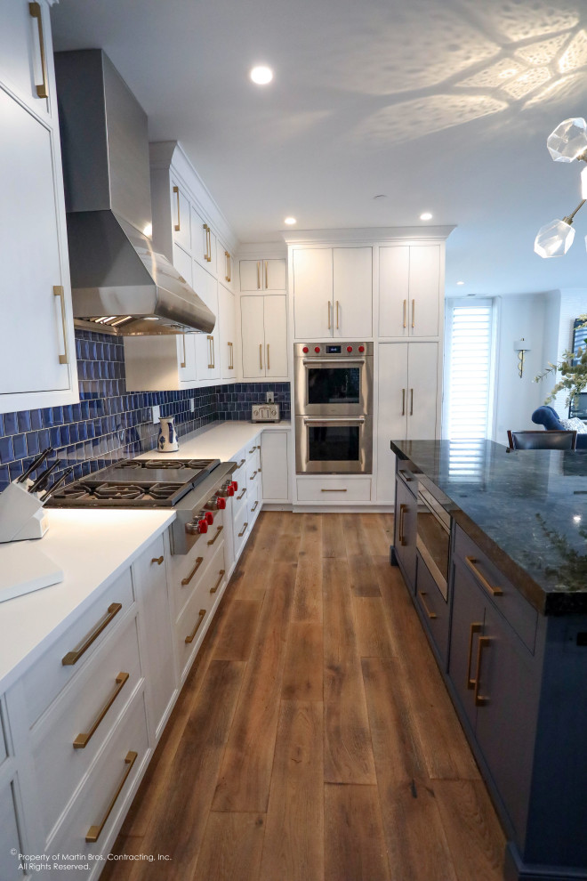 Example of a large transitional u-shaped medium tone wood floor open concept kitchen design with a single-bowl sink, flat-panel cabinets, white cabinets, quartz countertops, blue backsplash, glass tile backsplash, stainless steel appliances, an island and white countertops