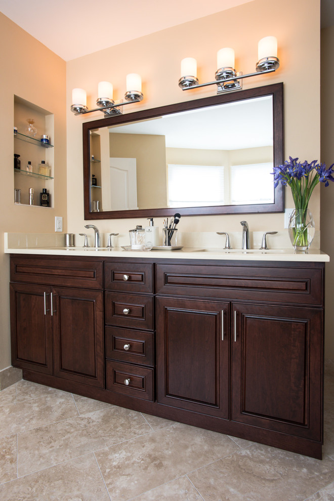 Large traditional master bathroom in Newark with raised-panel cabinets, dark wood cabinets, a freestanding tub, beige walls, travertine floors, an undermount sink, solid surface benchtops, beige floor, an alcove shower, a hinged shower door, beige tile and limestone.