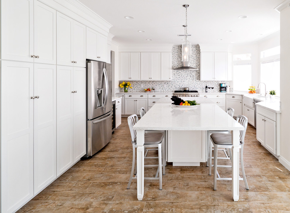 Design ideas for a mid-sized transitional u-shaped open plan kitchen in Orange County with a farmhouse sink, shaker cabinets, white cabinets, quartz benchtops, white splashback, porcelain floors and with island.
