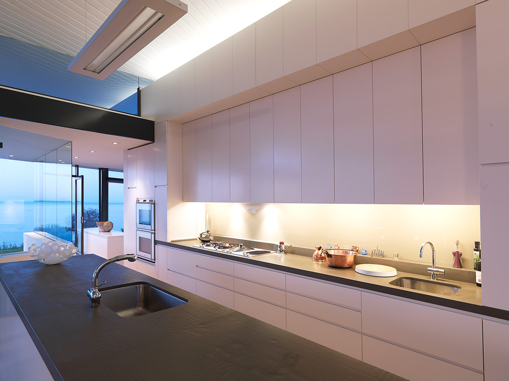 Inspiration for an expansive contemporary galley eat-in kitchen in Melbourne with an integrated sink, flat-panel cabinets, white cabinets, solid surface benchtops, stone slab splashback, stainless steel appliances and with island.